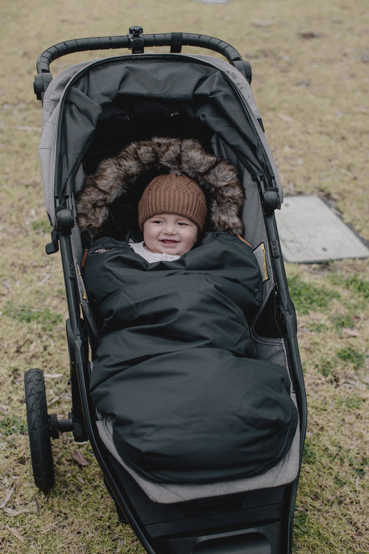 Nordic Footmuff Pram Liner in Classic Black with grey/brown fur, featuring brown leather details, reversible design for all seasons, and universal fit for all prams.