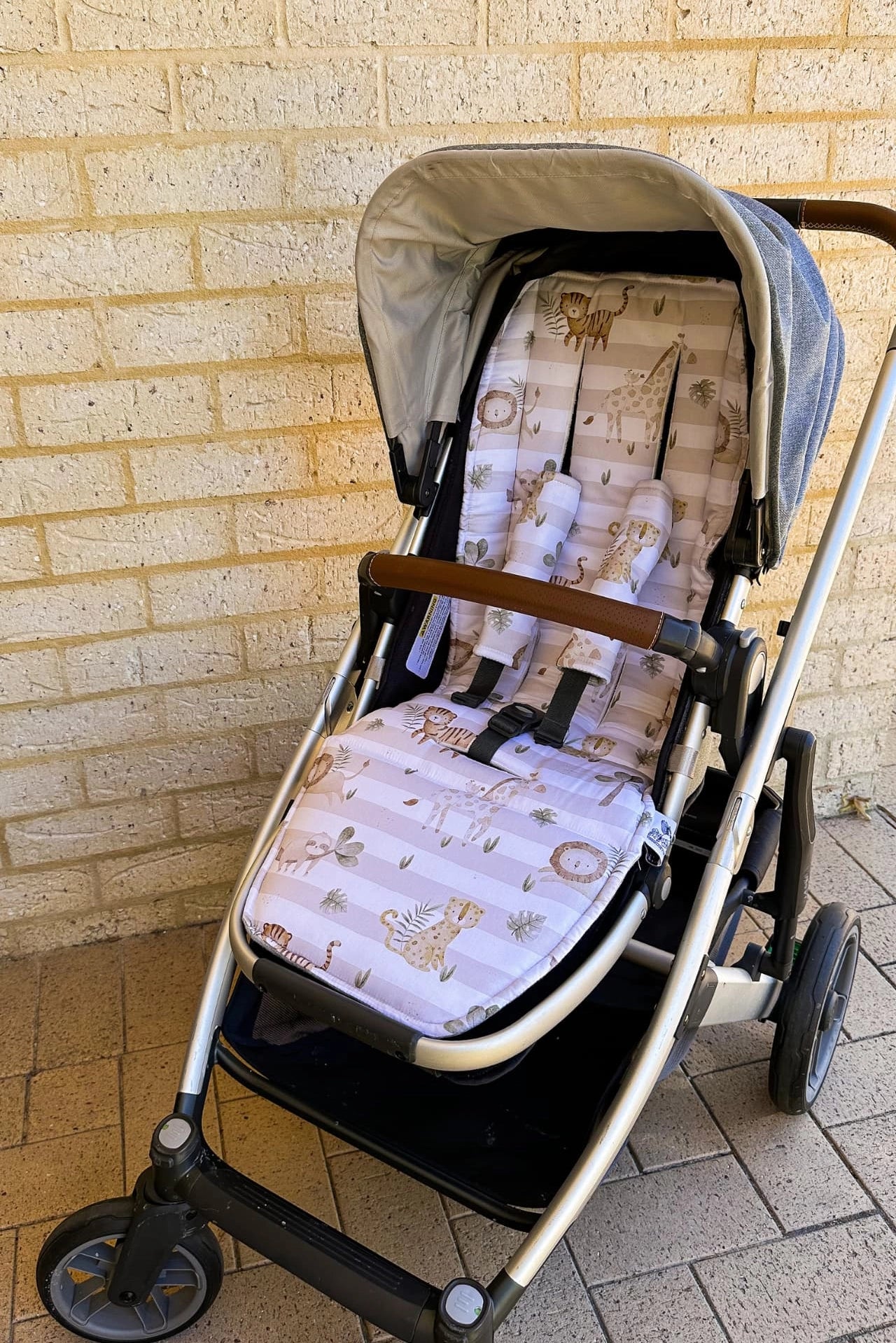 Universal Pram Liner - Safari applied to a pram, featuring a design with a sloth, giraffe, tiger, and lion. The liner is shown installed with matching shoulder strap covers, highlighting its fit and protective design on the pram seat.