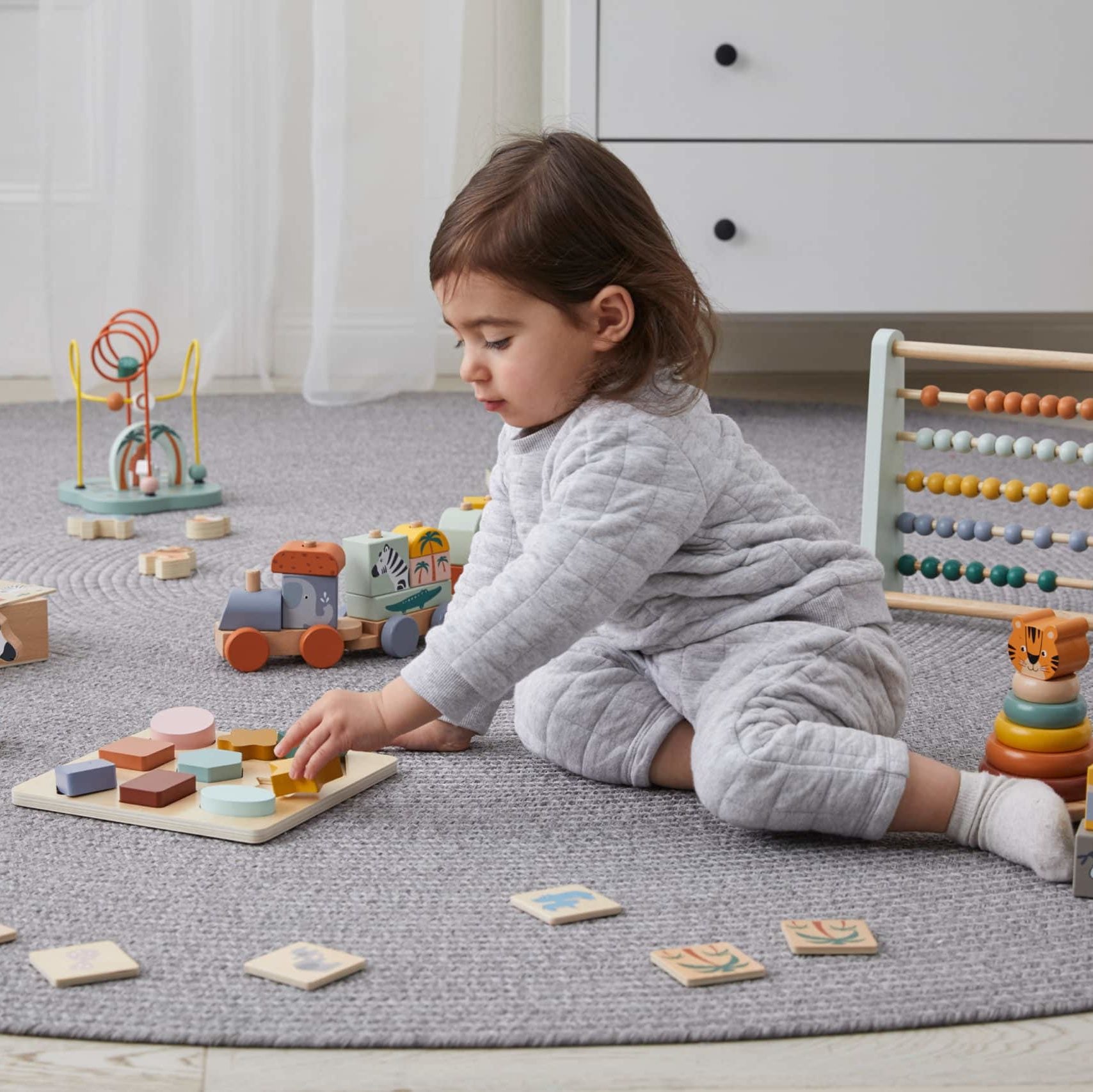 Wooden Shape Puzzle Toy with various shapes for children. Made from natural wood and non-toxic paint, suitable for kids 12 months and older. A child happily plays with the puzzle, learning shapes and coordination.