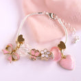 Load image into Gallery viewer, Fantasia Charm Bracelet by Lauren Hinkley displayed in a gift box, featuring two gold hearts, a pink bow with gold trim, a white flower with gold outline, a pink butterfly with gold outline, a large pink heart with gold glitter, and a bead pink
